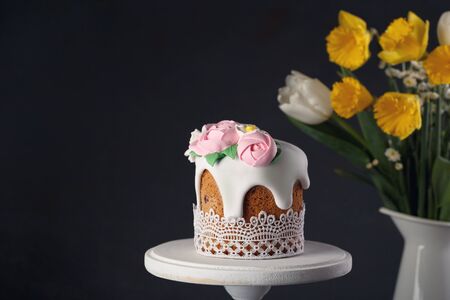 Homemade Easter cake on white wooden stand with bouquet of daffodils and tulips in vase on dark background. Holiday conceptの写真素材