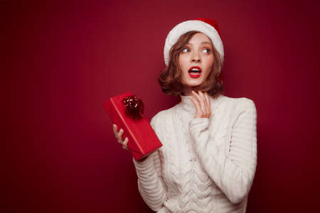 Dreamy woman in Santa hat with gift on red backgroundの写真素材