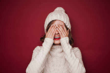 Cheerful smiling woman in sweater cover her eyesの写真素材