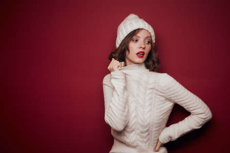 Dreamy woman in white knitted sweater hold collar on red backgroundの写真素材