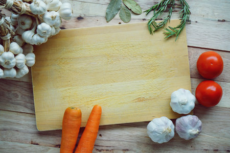 Many fresh ingredients, rosemary, spaghetti, carrot, tomato, garlic, onion and bay leaf on chopping board with wooden table background, copy space, cooking conceptの写真素材