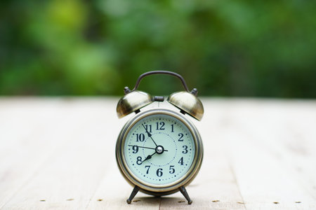 Analog alarm clock on wooden table with blur green garden background, 8 am., 8 o'clock, copy space