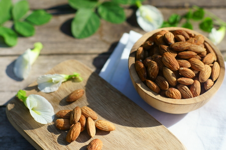 Almond nut in wooden bowl on wood table with nature green leaf background, copy spaceの写真素材
