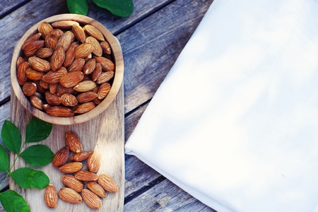 Almond nut in wooden bowl on wood table with nature green leaf background, copy spaceの写真素材