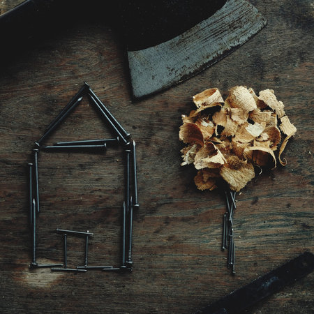 House made of nail and little tree made of wood dust on old wood background, creative artwork...