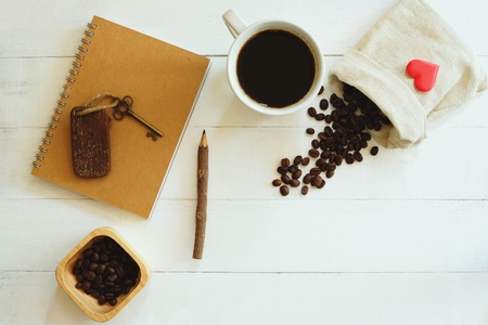 White cup of hot black coffee, brown notebook, pencil, vintage key, coffee bean decorated on white table background, casual work table conceptの写真素材