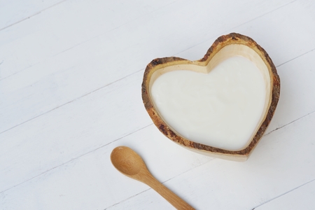 Plain organic yogurt in heart shape wooden bowl and wood spoon on white wood texture background, copy spaceの写真素材