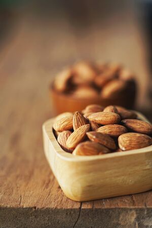 Almond nut in wooden bowl on wooden table with green leaf background, copy spaceの写真素材