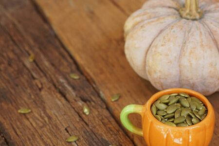 Pumpkin grain in pumpkin cup and fresh pumpkin fruit on classic wooden table background, cereal, copy spaceの写真素材
