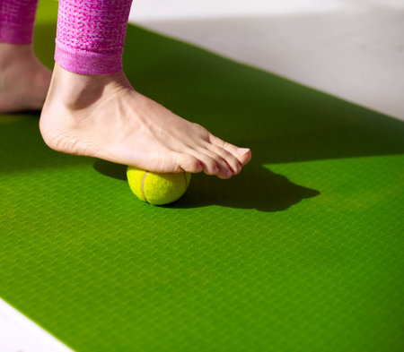 Tennis ball under female foot. Massage for relieve muscle tension, improve circulation, and plantar fasciitis relief. Physiotherapy, reflexology, and flexibility promotion concept.の写真素材