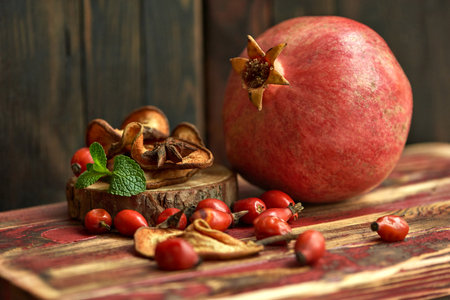 Ripe pomegranate, rosehip berries, dried apples, and mint leaves on a wooden surface. Ingredients for preparing healthy autumn hot tea. still life.の写真素材