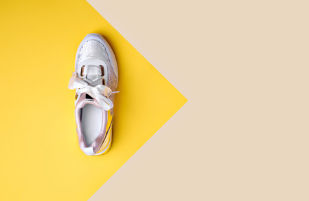Trendy sequin sneaker with white satin shoelaces isolated on a geometric yellow-beige background with pointing on copy space. Flat lay. Creative layout with footwear. Outlet marketing poster.の写真素材