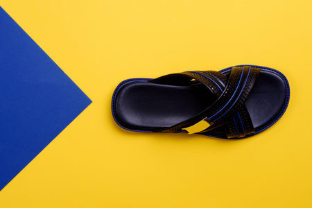 Stylish criss-cross black-blue men's slipper with embossing design isolated on a yellow-blue background with copy space. Fashion blogger content. Creative design for shoe store advertising poster.の写真素材