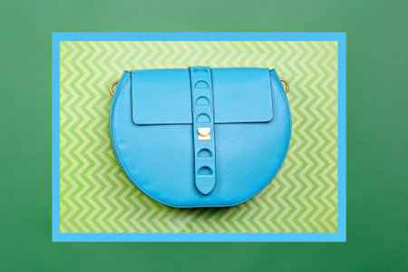 Trendy turquoise leather round-shaped woman's handbag with strap clasp isolated on a creative green-blue background with a zigzag pattern. Fashion blog. Summer accessories sale campaign, retail.の写真素材