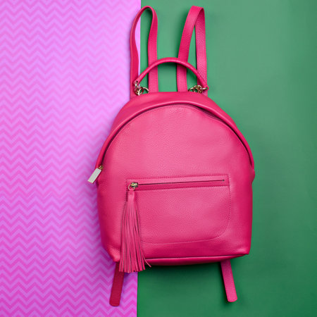 Contemporary women's pinkish-red leather backpack with a handle and zipped compartment with tassel pull isolated on a fun contrasting pink-green background. Mock-up for online fashion store or blog.の写真素材