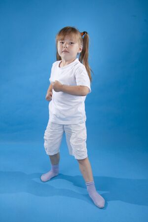 Small serious girl is posing as fighter isolated on blue backgroundの写真素材