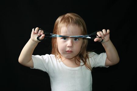 Little girl with scissors. Black background.の写真素材
