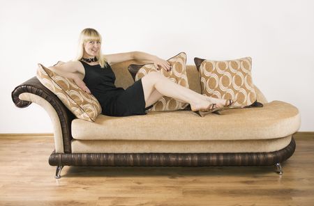 Blond girl sits on the sofa against the background of the white wallの写真素材