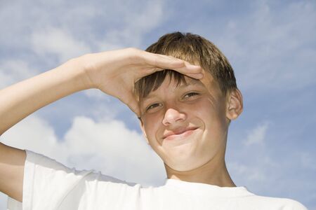 Happy lad portrait shadowing his eyes from the bright light of the sunの写真素材