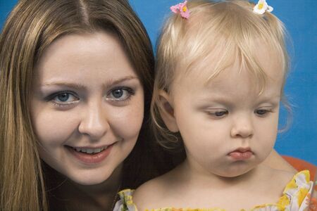 Young and beautiful mother with her sweet little daughter isolated on blue.