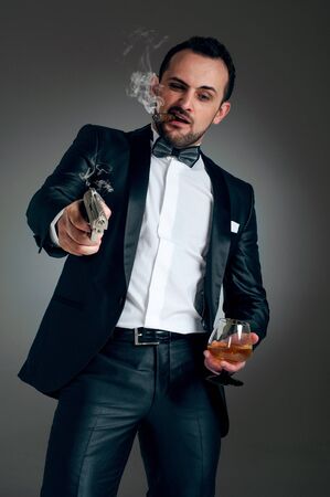 Cool man in a suit with a cigar, gun and glass with alcoholic beverage