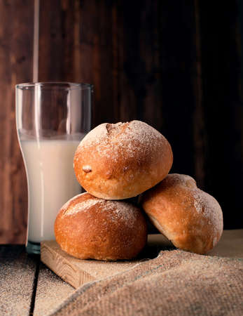 Freshly baked buns and glass of milk on wooden boardの写真素材