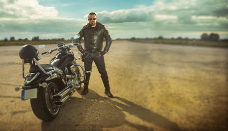 Biker in leather jacket standing by a motorcycle.の写真素材