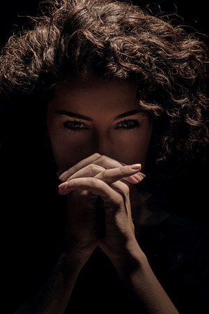Close up portrait of young beautiful brunette woman with folded handsの写真素材
