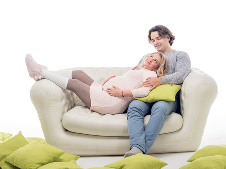 Pregnant fasion woman in knitted sweater with husband sitting on the sofaの写真素材