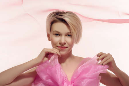 Beautiful young blonde naked woman in big pink bow on background