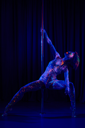 Female pole dancer in bright neon colours under ultraviolet (UV) light on backgroundの写真素材