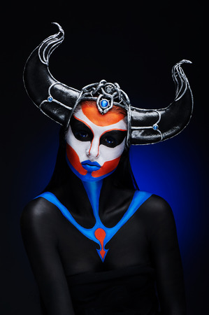 Mystery portrait of female faun with blue eyes, body art and silver snakes on black hornsの写真素材