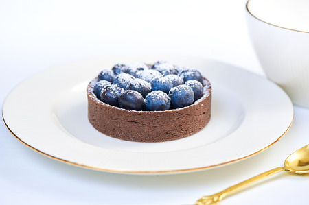Hand made dessert tarlets from pistachio and chocolaty bakery dough with blueberry decoration served on plate with cap of teaの写真素材
