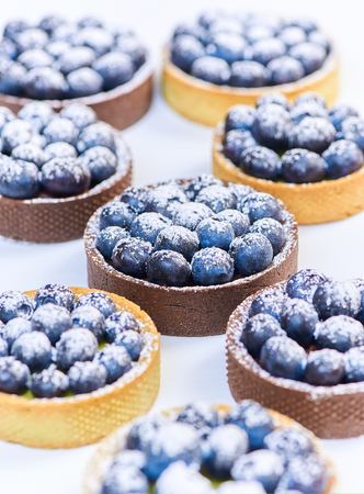 Hand made tarlets dessert from pistachio and chocolaty bakery dough with blueberry decoration on white backgroundの写真素材