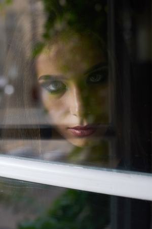 Unhappy beautiful brunette woman with make up looking through window