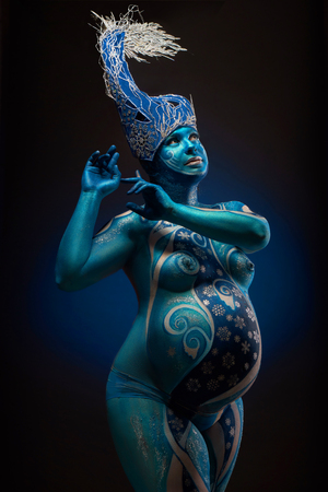 Beautiful pregnant woman with headwear and abstract body art in shades of blue and white の写真素材