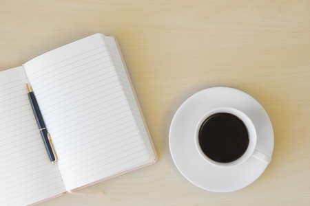 Top view of cup of coffee, blank notebook and pen on wooden tableの写真素材