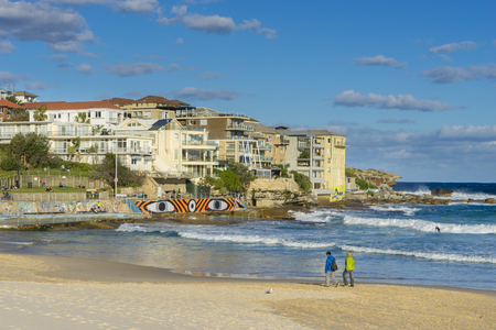 Sydney, Australia - June 25, 2016: View of people walking along the beach and modern apartments at Bondi Beach during daytime. Bondi Beach is one of the most famous beaches in Australia.のeditorial素材