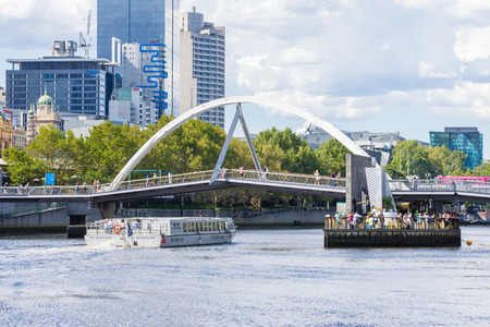 Melbourne, Australia - March 17, 2016: View of floating bar under the Yarra Pedestrian Footbridge and cruise boat with skyscrapers behind it in Melbourne during daytime.のeditorial素材