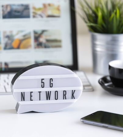 5G network lightbox on office table with computer, smartphone, coffee and potted plant.の写真素材