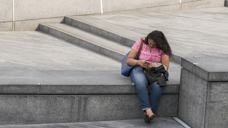 Lady using mobile phone sitting on a parapet near Tower Bridge in London, UKの写真素材