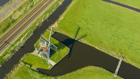 Aerial view of a old dutch traditional windmill on the rural countryside in The Netherlands with a dike, canals. railway. bridge and a road.の写真素材