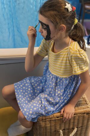 A young girl from poor deprived family is entertaining herself by face paintingの写真素材