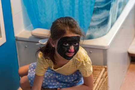 A young girl from poor deprived family is entertaining herself by face paintingの写真素材