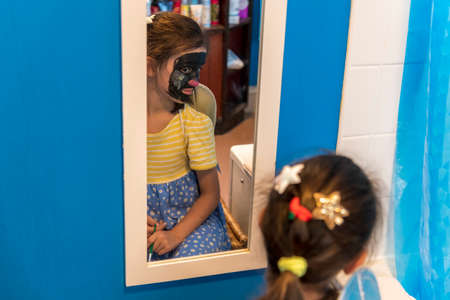 A young girl from poor deprived family is entertaining herself by face paintingの写真素材