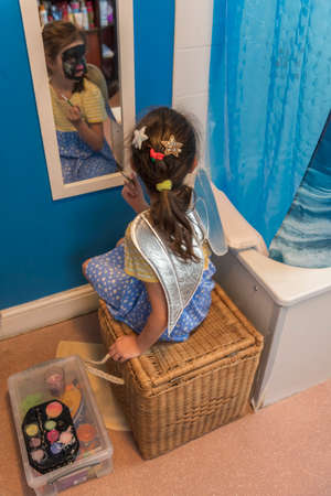 A young girl from poor deprived family is entertaining herself by face paintingの写真素材