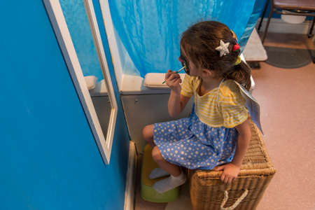 A young girl from poor deprived family is entertaining herself by face paintingの写真素材