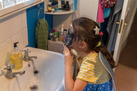 A young girl from poor deprived family is entertaining herself by face paintingの写真素材