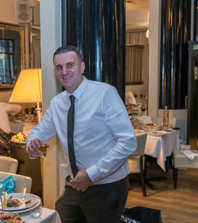 Portrait of handsome young happy man smiling and drinking vodka in restaurant, London, UKの写真素材