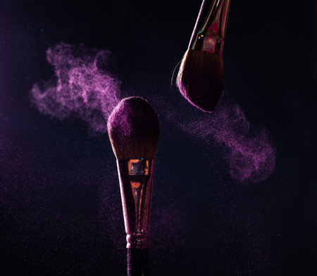 Make-up brushes with pink or violet powder explosion on dark backgroundの写真素材